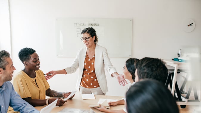 female leader standing up around a table and turned towards her team of 5 