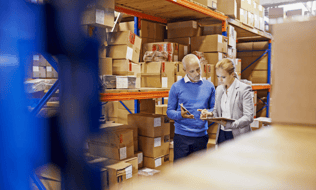 a man and a woman standing in a warehouse looking at an inventory sheet